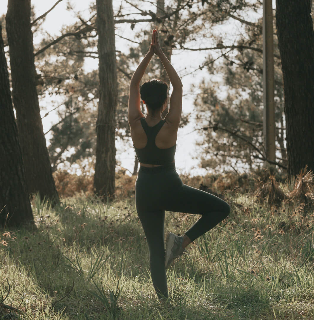 Frau beim Yoga in der Baum-Pose im Wald, achtsam und naturverbunden.